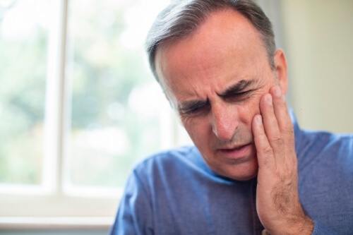 Man in blue shirt holding his cheek in pain