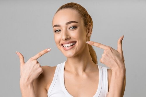 Young woman pointing to her smile after teeth whitening in Pecan Grove